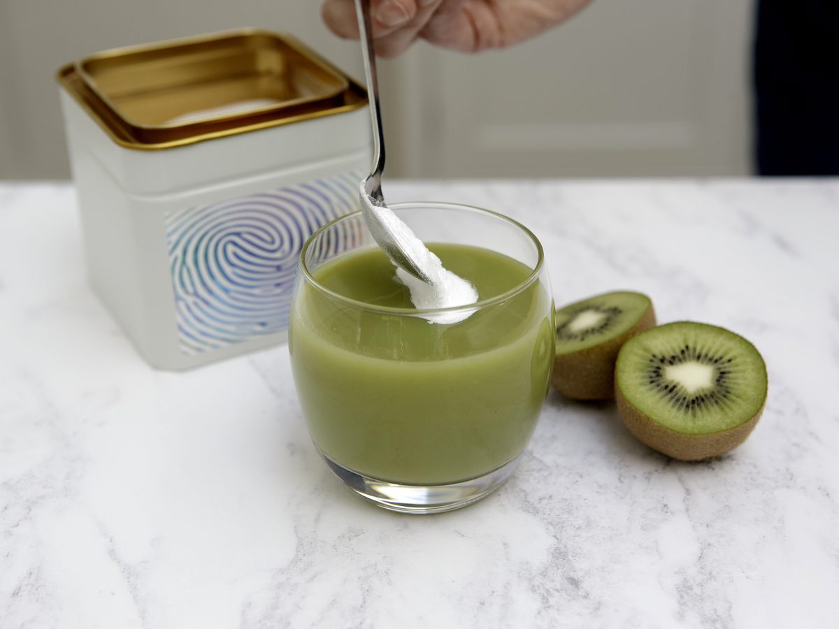 A scoop of the blend stirred into a green smoothie beside the open tin